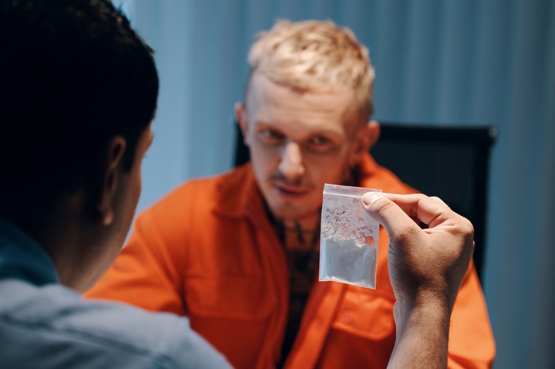 Detective showing criminal small bag with white powder as evidence